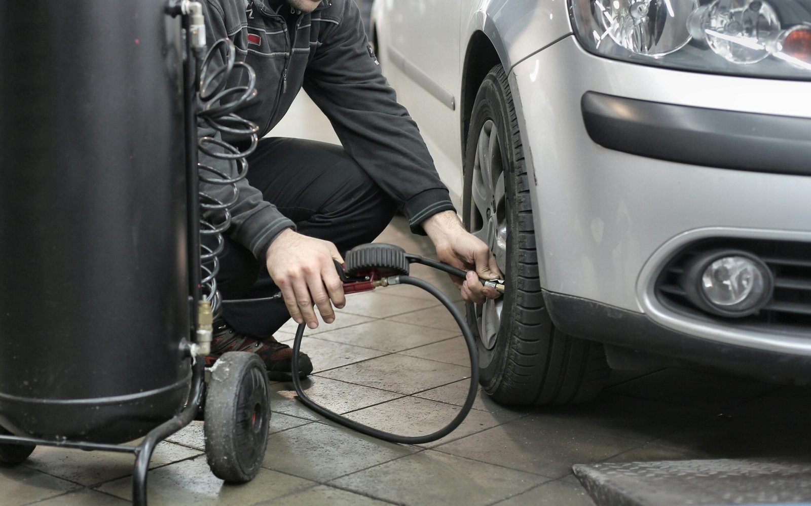 Mechanic inspecting and adjusting tire pressure in an auto repair shop.